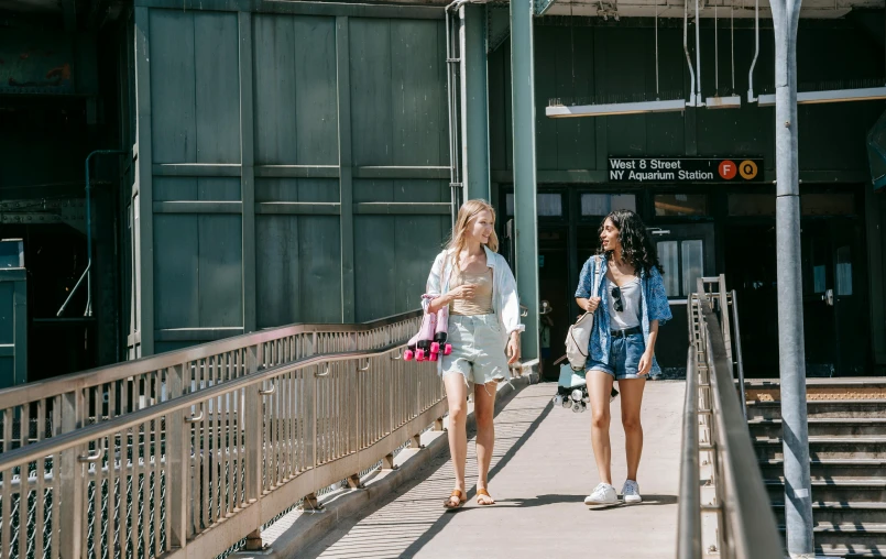 a couple of women walking down a sidewalk, pexels contest winner, train station in summer, college students, overpass, sydney park