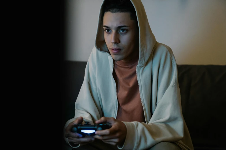 a man sitting on a couch holding a game controller, beige hoodie, looking distracted, **cinematic, saadane afif