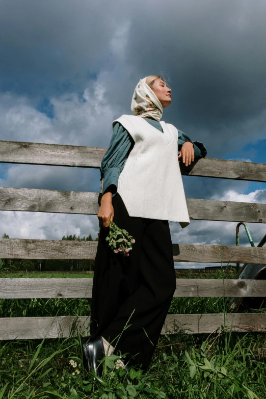 a woman standing in front of a wooden fence, inspired by August Sander, unsplash, renaissance, hijab, swedish countryside, model is wearing techtical vest, nordic summer