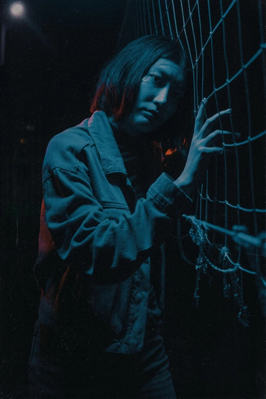 a woman leaning against a fence at night, inspired by Elsa Bleda, pexels contest winner, conceptual art, 8 0 s asian neon movie still, portrait of sadako of the ring, ((chains)), standing in a dimly lit room