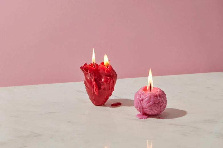 two candles sitting next to each other on a table, a surrealist sculpture, inspired by Marina Abramović, vanitas, featuring pink brains, flaming heart, gooey, frontal shot