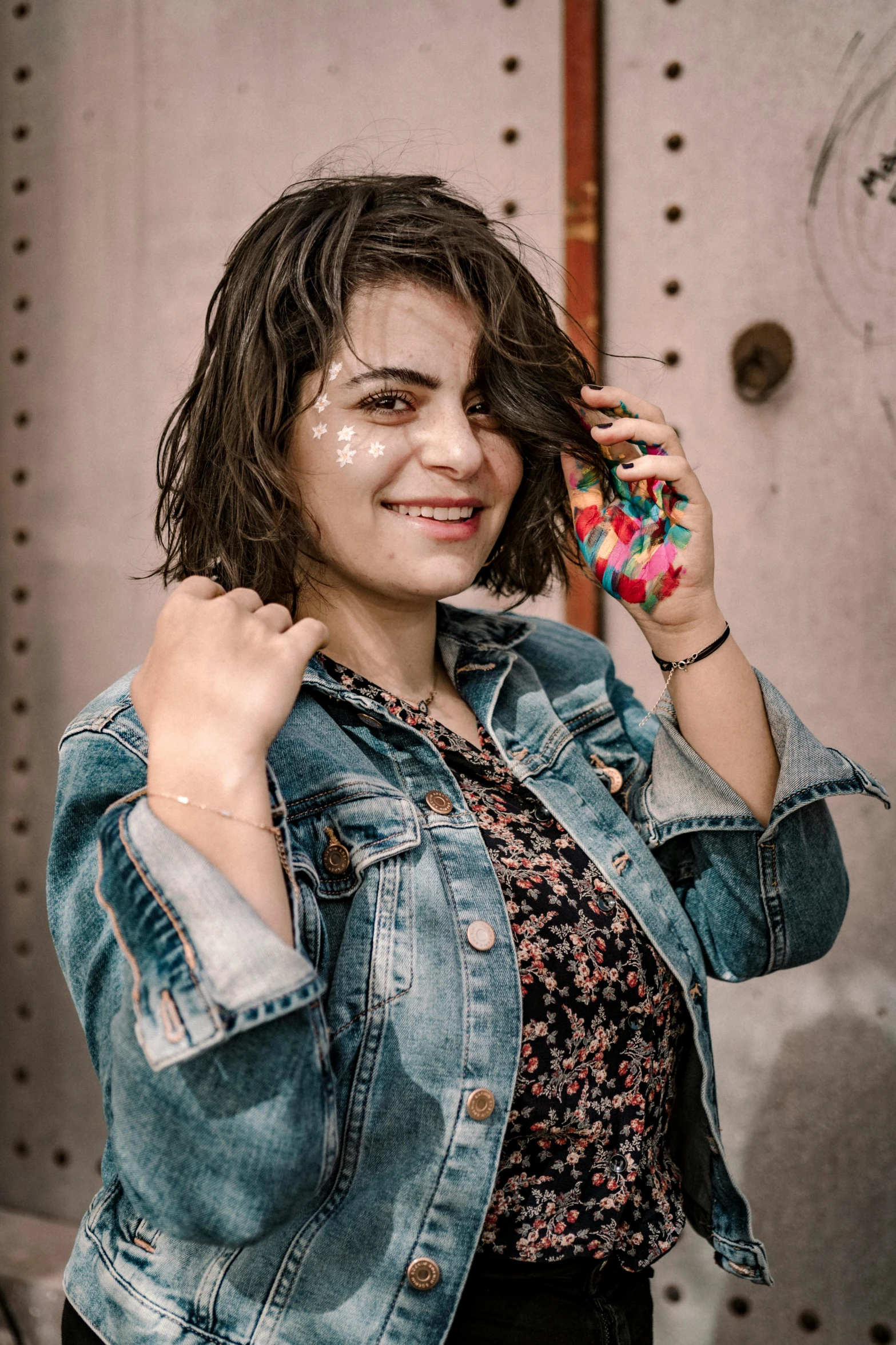 a woman in a denim jacket talking on a cell phone, inspired by Elsa Bleda, trending on pexels, graffiti, dark short curly hair smiling, confetti, fair olive skin, posing for a picture