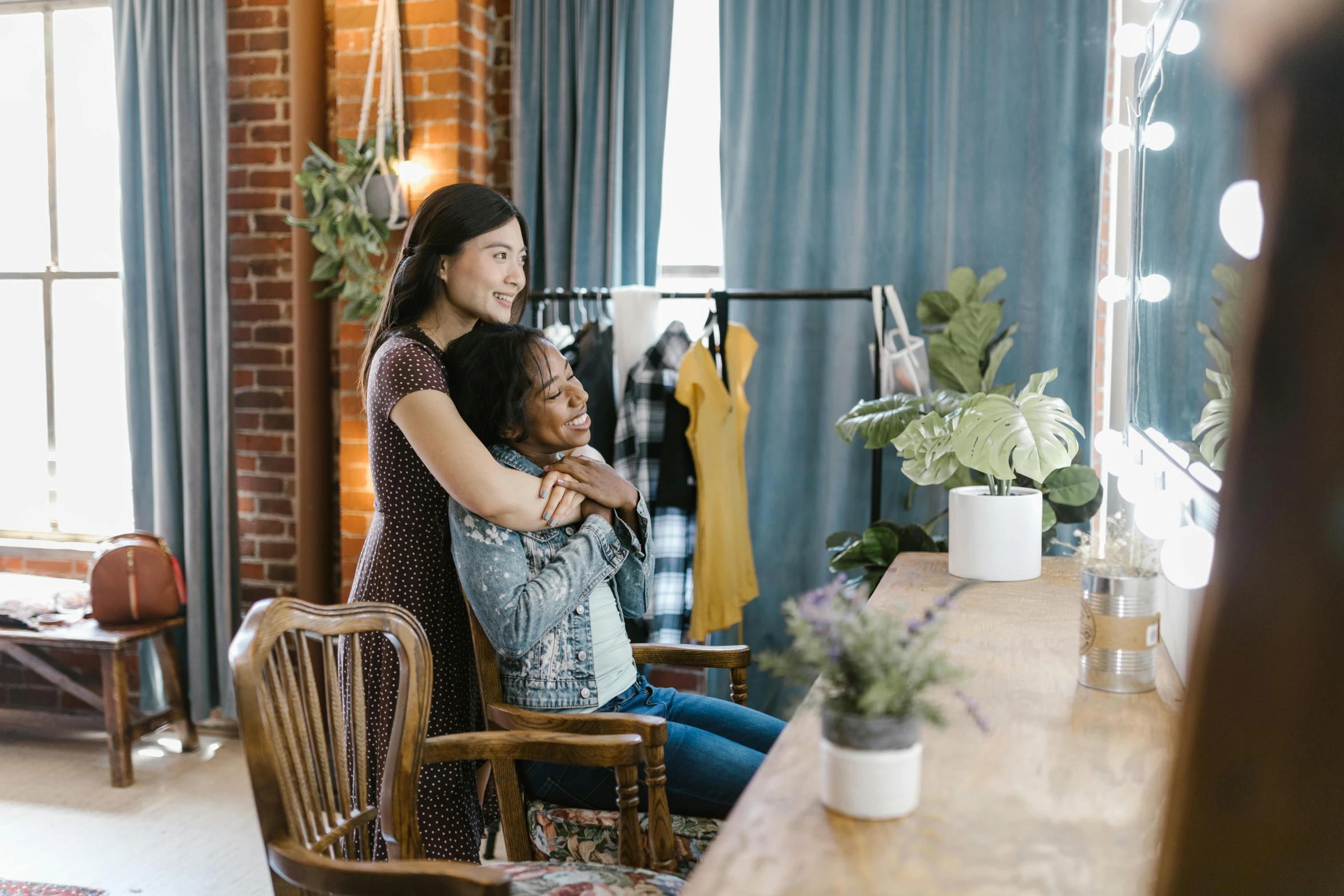 a woman sitting on a chair in front of a mirror, hugging each other, portrait featured on unsplash, flower shop scene, earing a shirt laughing