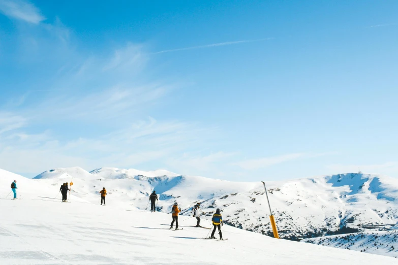 a group of people riding skis down a snow covered slope, by Peter Churcher, pexels contest winner, arrendajo in avila pinewood, looking at the mountains, golden detailing, on a bright day