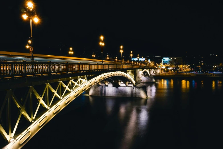 a bridge over a body of water at night, by Adam Szentpétery, pexels contest winner, art nouveau, hungarian, yellow lights, high contrast of light and dark, long exposure outside the city