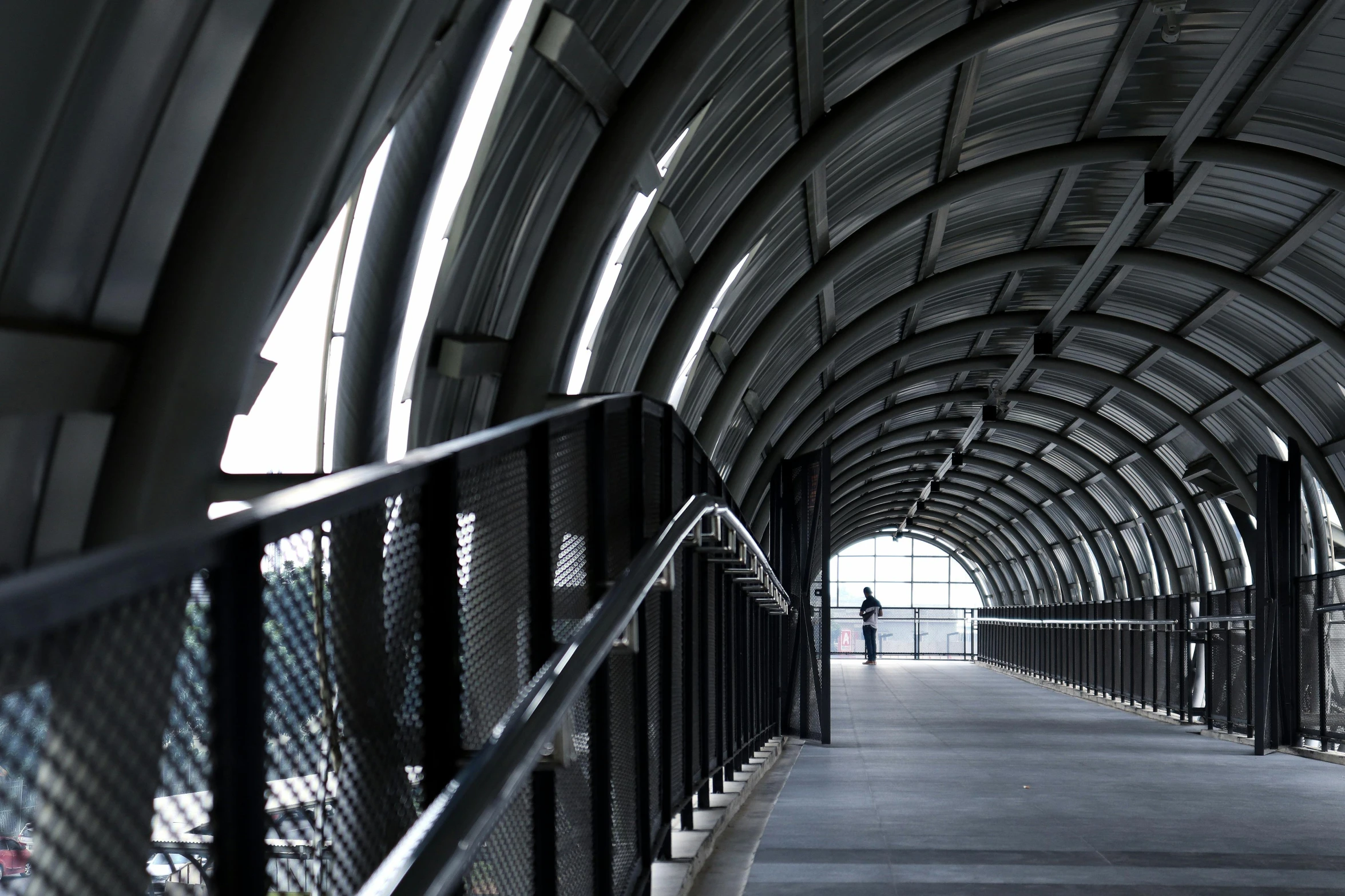 a black and white photo of a walkway, inspired by Tadao Ando, unsplash contest winner, steel archways, person in foreground, panoramic anamorphic, alessio albi