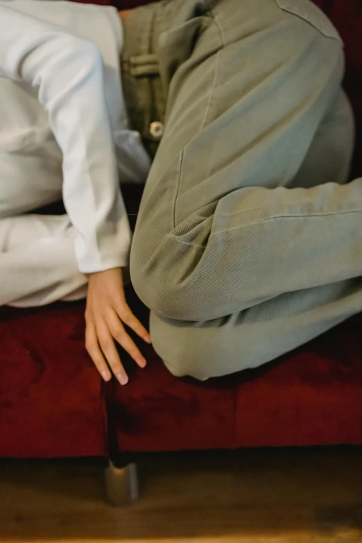 a man laying on top of a red couch, by Nina Hamnett, unsplash, visual art, green corduroy pants, woman holding another woman, knobbly knees, spasms