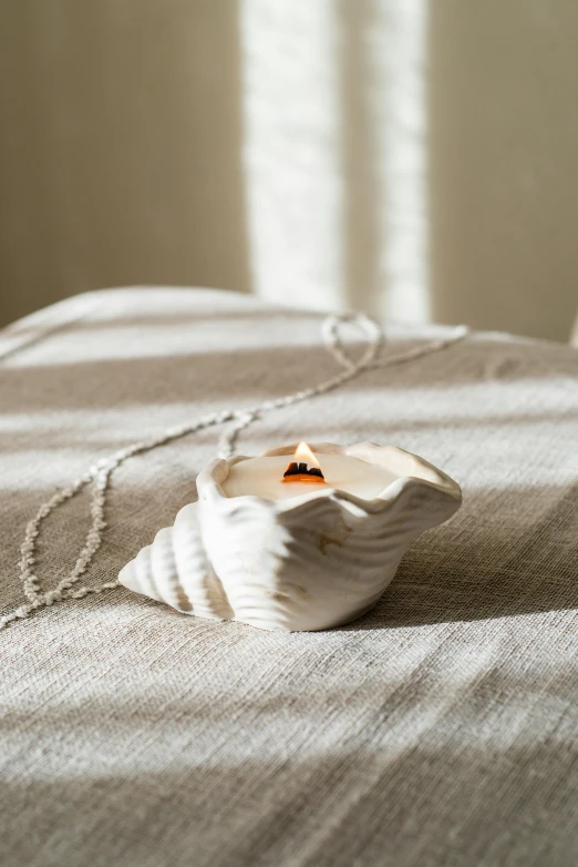 a white shell sitting on top of a bed, by Nina Hamnett, unsplash, small necklace, on a candle holder, ignant, highly detailed product photo