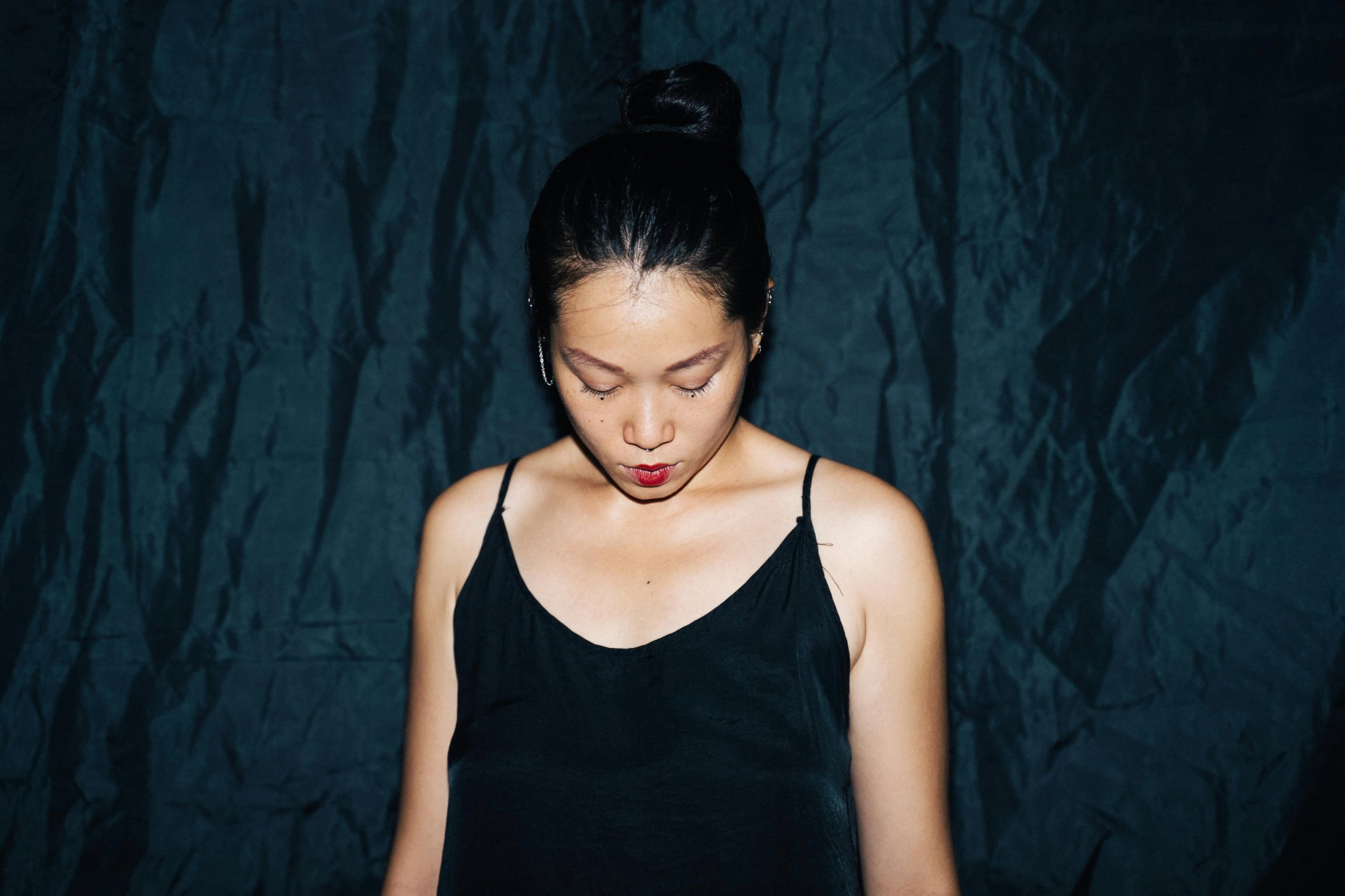 a woman standing in front of a black background, an album cover, inspired by Ruth Jên, unsplash, minimalism, beautiful asian woman sitting, sleepy expression, taken in the late 2000s, wearing a camisole