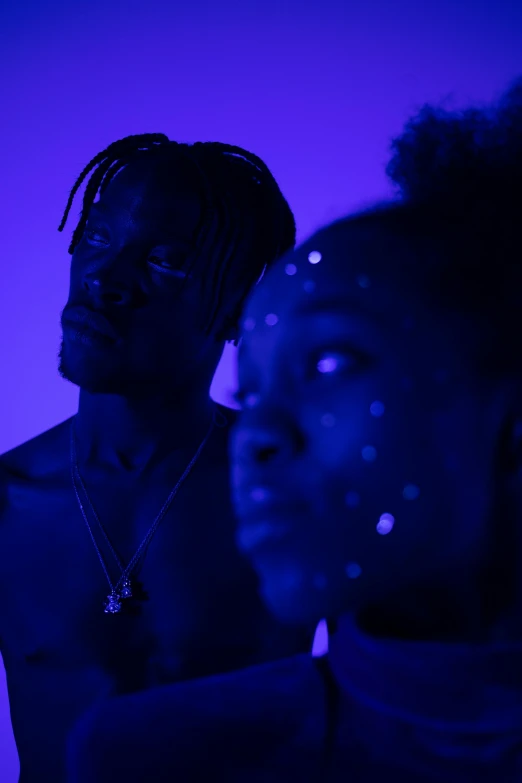 a man and a woman standing next to each other, an album cover, trending on pexels, afrofuturism, blue lights and purple lights, playboi carti portrait, ( ( theatrical ) ), deep blue skin