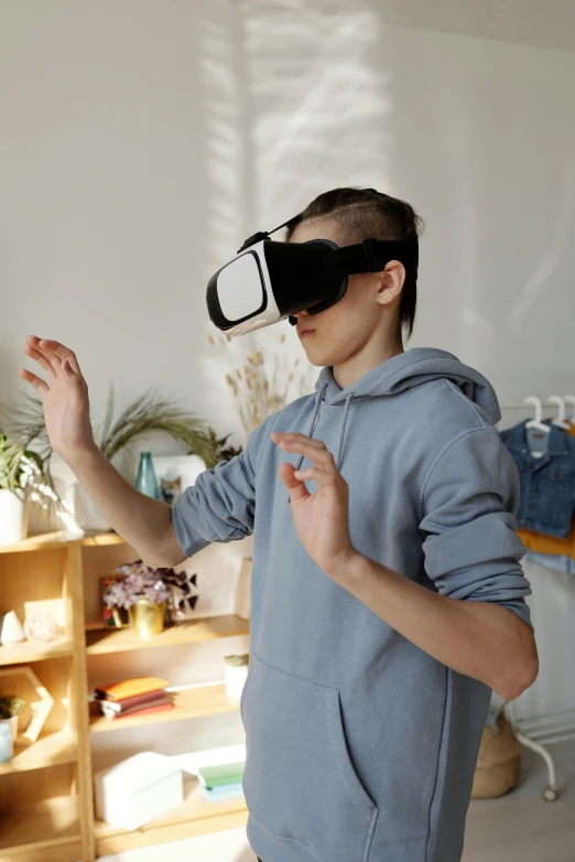 a man standing in a living room wearing a pair of virtual glasses, trending on pexels, teenage boy, waving, educational, wearing futuristic clothing