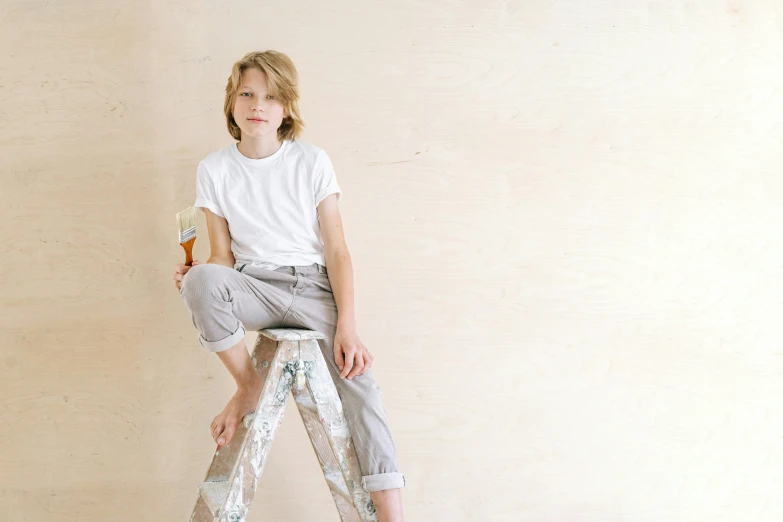 a little boy that is sitting on a ladder, inspired by Sarah Lucas, pexels contest winner, white paint, male teenager, brown pants, beautiful wallpaper