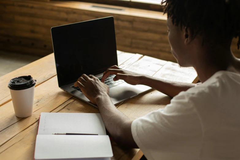 a man sitting at a table using a laptop computer, by Carey Morris, pexels, afro tech, bottom angle, student, official screenshot