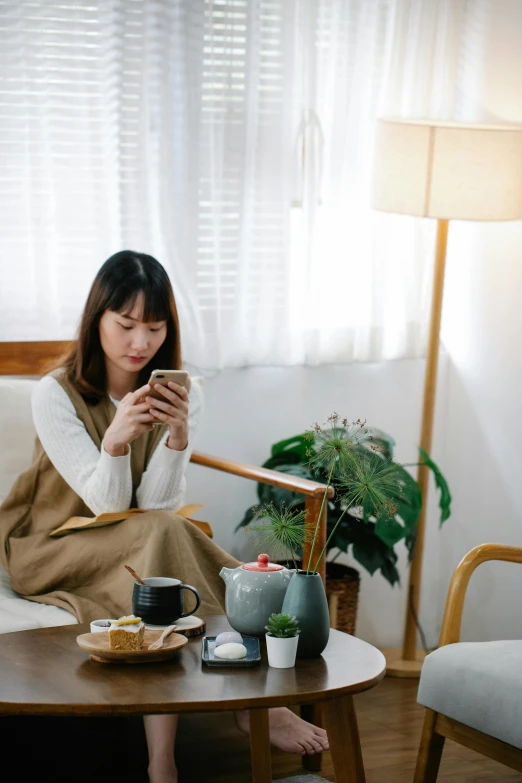 a woman sitting on a couch looking at her phone, by Jang Seung-eop, drinking tea, japanese collection product, brightly lit room, brown