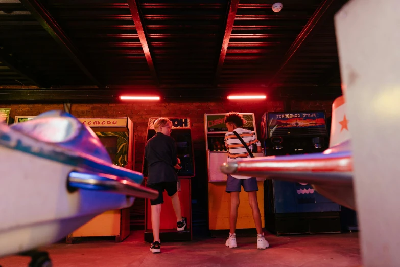 a couple of people that are standing in a room, by Lee Loughridge, pexels contest winner, interactive art, 80s outdoor retro arcade, kids playing, blue and red lights, dingy gym