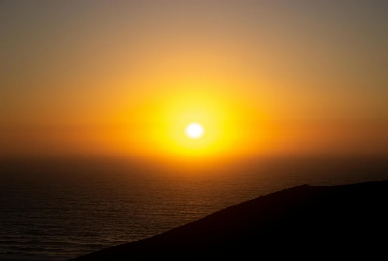 a person standing on top of a hill next to the ocean, by Daniel Lieske, pexels contest winner, happening, bright yellow and red sun, hollister ranch, it's getting dark, an expansive view of the sun