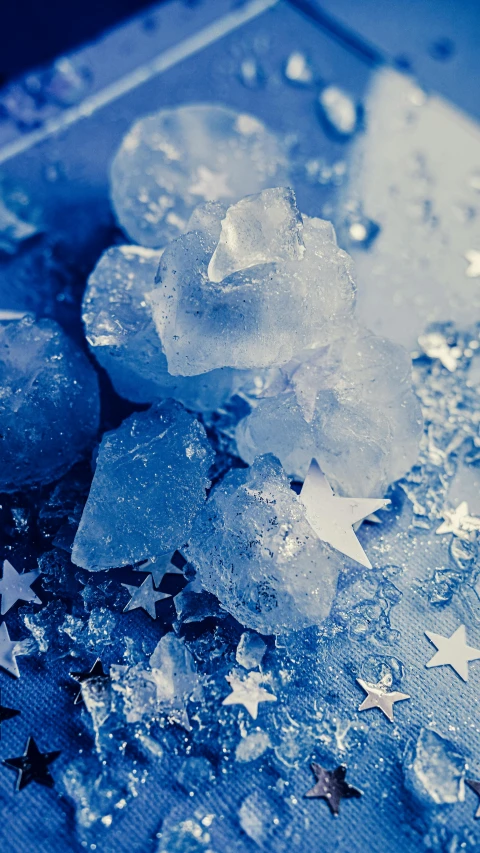 a pile of ice sitting on top of a table, an album cover, by Adam Marczyński, trending on unsplash, crystal cubism, rugged | stars, blue crystals, grainy, stars and planets