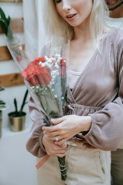 a woman standing next to a man holding a bunch of flowers, a colorized photo, pexels contest winner, soft grey and red natural light, glossy surface, flower shop scene, photo of a rose