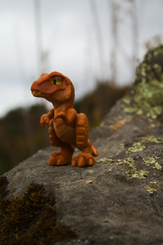 a toy dinosaur sitting on top of a rock, inspired by Adam Rex, pocket monster companion, brown scales, overlooking, claymation