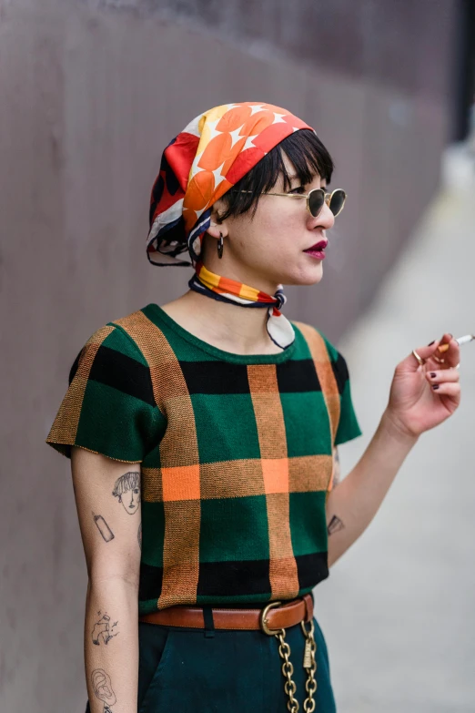 a woman standing on a sidewalk smoking a cigarette, inspired by Ren Hang, trending on pexels, colorful bandana, pixie cut, checkered motiffs, green and orange theme