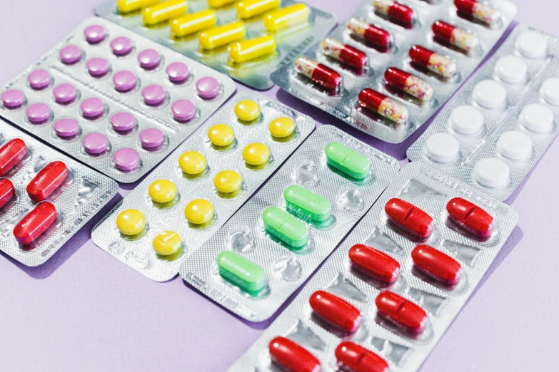 a bunch of pills sitting on top of a table, some red and purple and yellow, collection product, shields, lined up horizontally