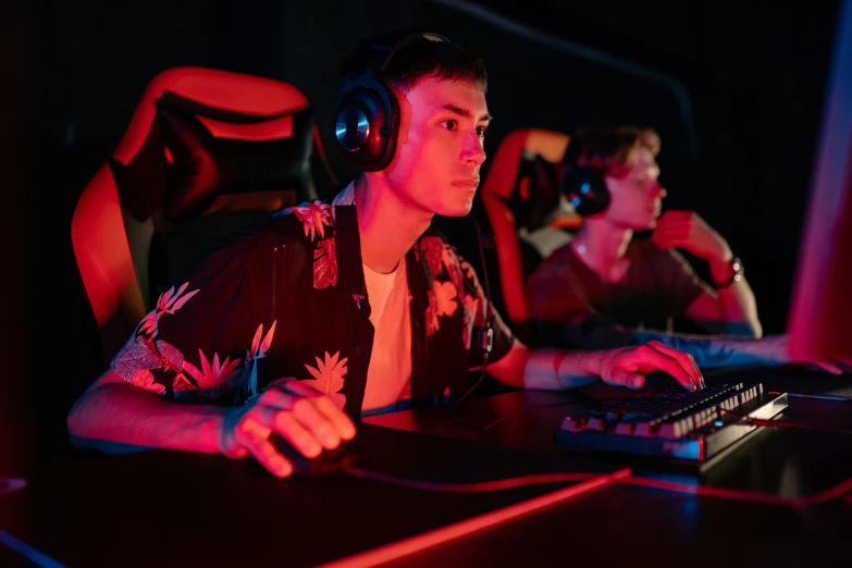 a man sitting in front of a computer with headphones on, pexels, realism, riot games, arcade machines, medium shot of two characters, orange and red lighting