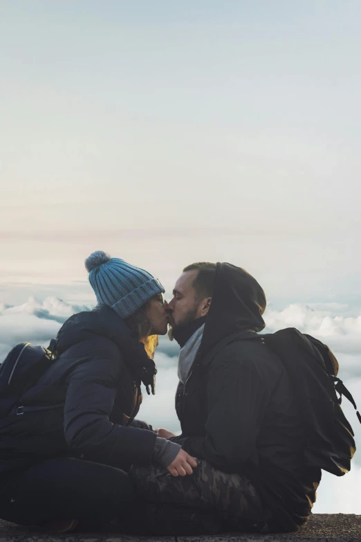 a man and woman sitting on top of a mountain, pexels contest winner, romanticism, kissing together, view above the clouds, 85mm lens”, winter setting