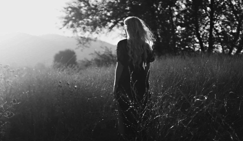 a woman standing in a field of tall grass, a black and white photo, tumblr, walking into a deep dark florest, blonde woman, in the hillside, during dawn