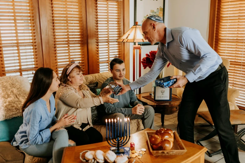 a man handing a menorah to a group of people, a colorized photo, pexels contest winner, holding gift, avatar image, happy family, cozy