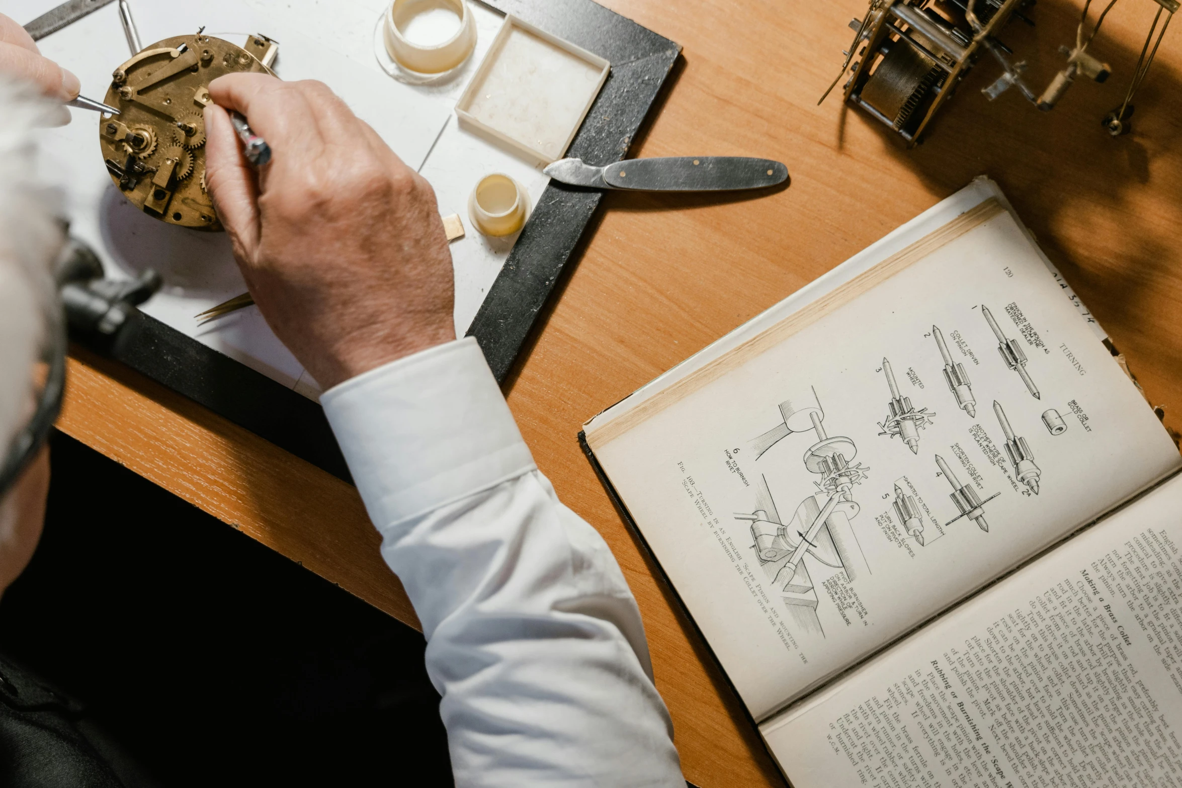 a man that is sitting at a table with a clock, trending on pexels, arts and crafts movement, surgical implements, with book of science, professional gunsmithing, technical drawings