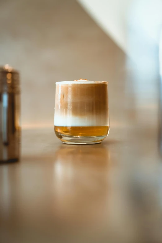 a glass filled with liquid sitting on top of a wooden table, aussie baristas, gold, thumbnail, cafe racer