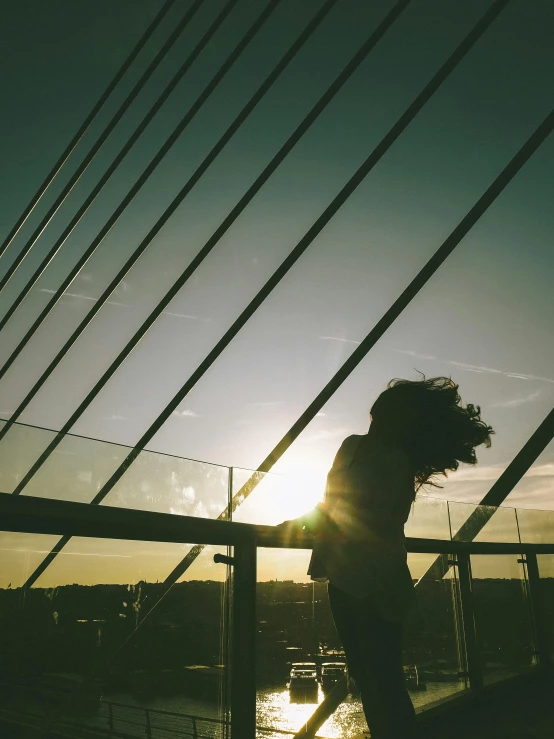 a person walking across a bridge at sunset, pexels contest winner, happening, windy hair, on rooftop, sassy pose, trending on vsco