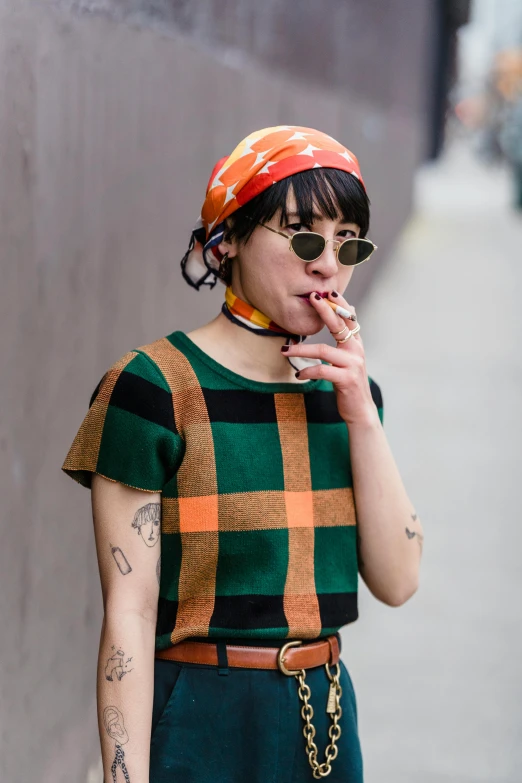 a woman standing on a sidewalk smoking a cigarette, an album cover, inspired by Winona Nelson, trending on pexels, checkered spiked hair, orange and green power, at new york fashion week, japanese