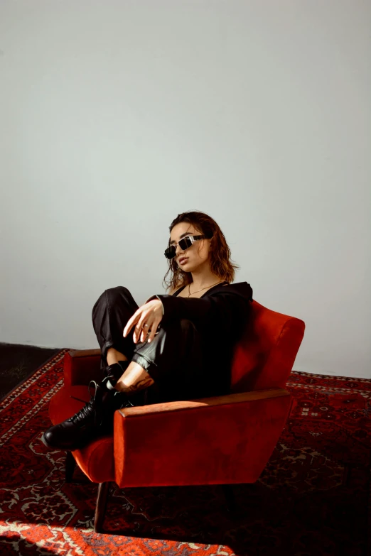 a woman is sitting in a red chair, an album cover, inspired by Elsa Bleda, trending on pexels, antipodeans, leather pants, sunglasses, warpaint aesthetic, isabela moner