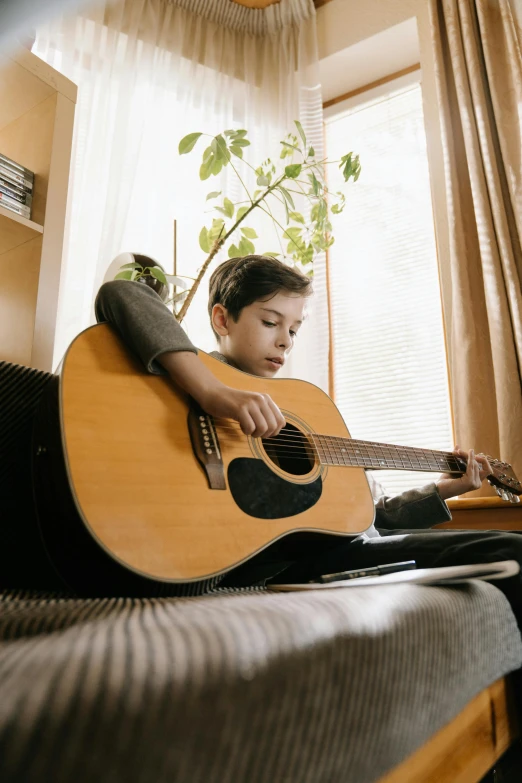 a young boy sitting on a couch playing a guitar, an album cover, pexels, sitting on a window sill, thumbnail, australian, school class