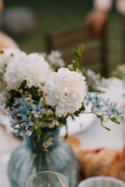 a vase filled with white flowers sitting on top of a table, by Jessie Algie, unsplash, amber and blue color scheme, al fresco, celebration, detail shot