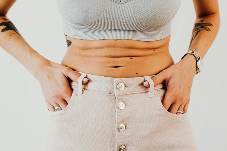 a woman standing with her hands in her pockets, trending on pexels, aestheticism, physical : tinyest midriff ever, belly button showing, varying detailed skin, toned colours