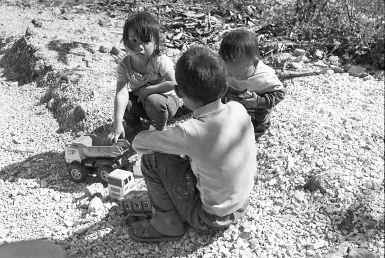 a group of children sitting on top of a pile of rocks, by Jim Nelson, flickr, mingei, broken toys are scattered around, gravel, tomoyuki yamasaki, three