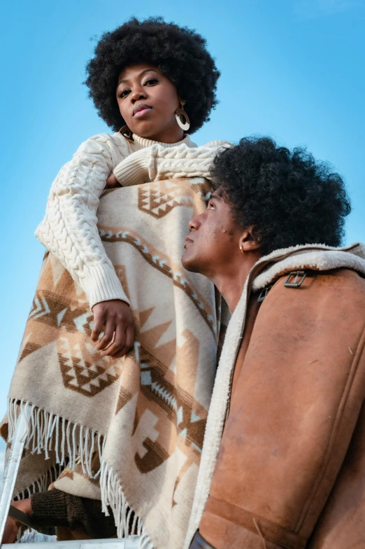 a man and a woman sitting on the back of a truck, by Carey Morris, trending on pexels, renaissance, wearing desert poncho, african american woman, brown sweater, promotional image