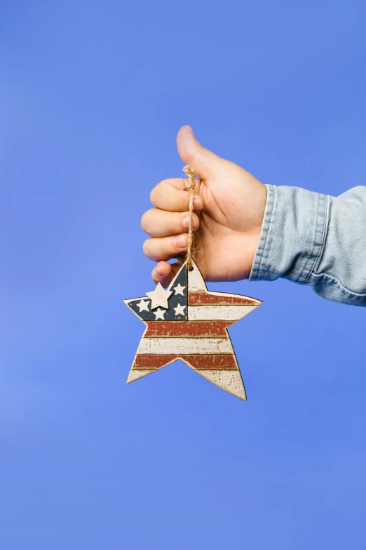 a person holding a wooden star ornament, stars and stripes, thumbs up, medium, environmental shot