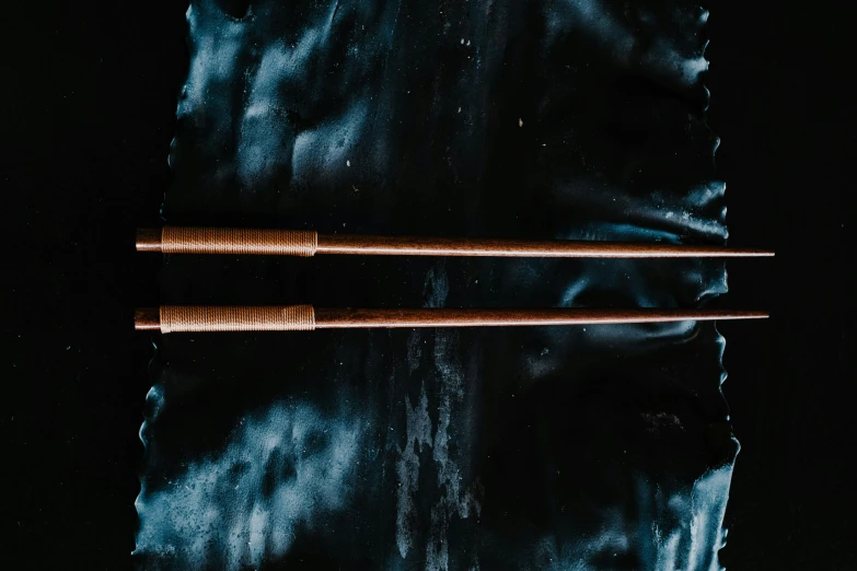 a pair of chopsticks sitting on top of a piece of paper, an album cover, inspired by Inshō Dōmoto, unsplash, purism, burnt umber and blue, body of water, magic wooden staff, intense atmospheric