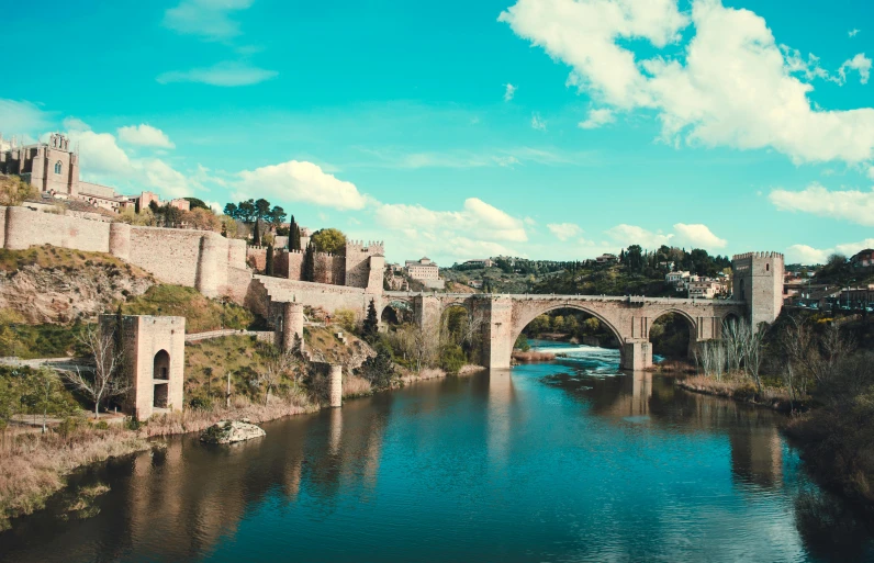 a bridge over a river with a castle in the background, a tilt shift photo, pexels contest winner, renaissance, in spain, sky blue, retro stylised, thumbnail