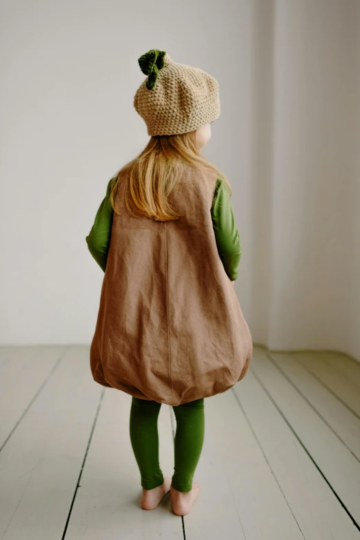 a little girl standing on top of a wooden floor, inspired by Elsa Beskow, unsplash, renaissance, deerstalker, green and brown clothes, model is wearing techtical vest, carrying big sack