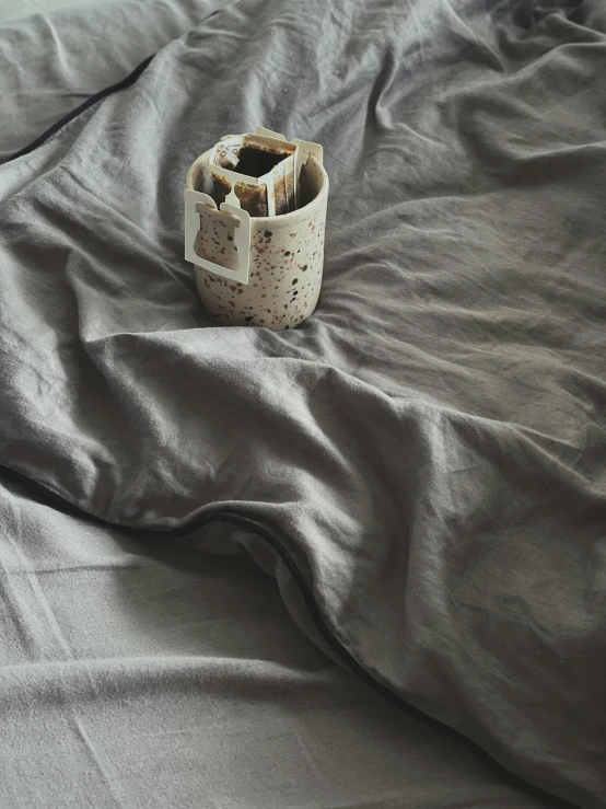 a cup of coffee sitting on top of a bed, in gunmetal grey, detail shot, wrinkled, made of glazed