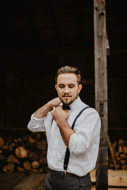 a man standing in front of a pile of wood, a colorized photo, trending on pexels, black bowtie, groom, chiseled jawline, liam