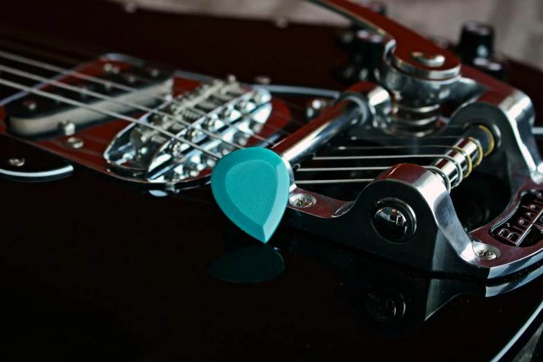a close up of a guitar with a guitar pick, by Joe Bowler, pexels contest winner, hurufiyya, teal color graded, connected to heart machines, product introduction photo, cyber augmentation implant