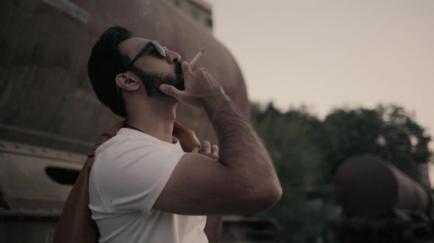 a man smoking a cigarette next to a train, pexels contest winner, hyperrealism, video still, confident relaxed pose, smokey background, ( ( theatrical ) )