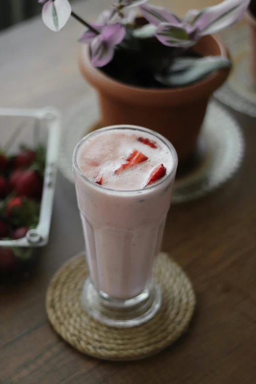 a drink sitting on top of a table next to a bowl of strawberries, milkshake, bangalore, seasonal, pink
