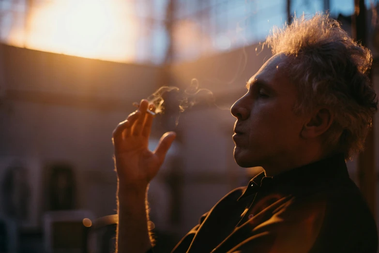 a close up of a person holding a cigarette, a portrait, inspired by John Cale, pexels contest winner, sun behind him, afternoon hangout, light from right, blonde man