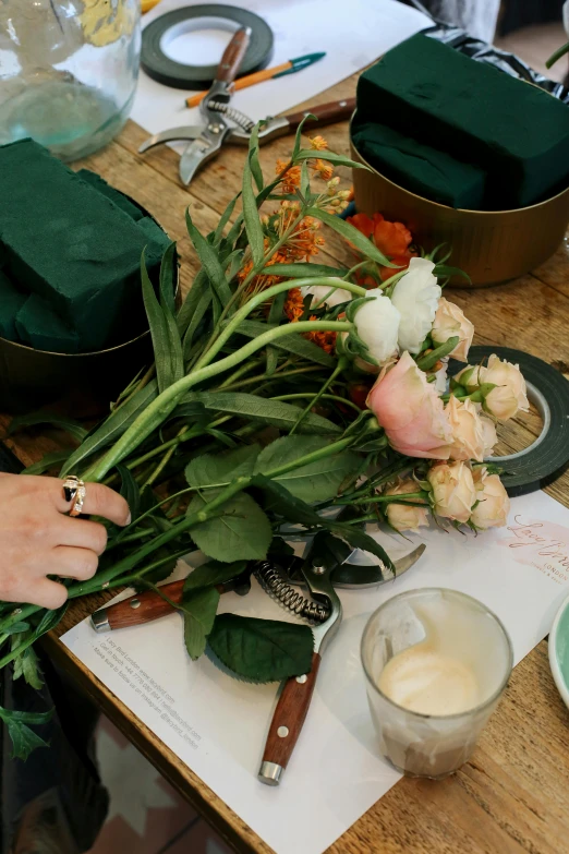 a person sitting at a table with a bunch of flowers, copper and emerald, ingredients on the table, back towards camera, maintenance